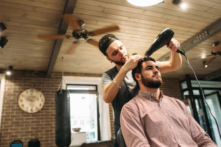Stylist drying clients hair at salon free space. Confident businessman making hairdo. Beauty, style, modern life concept. Barbershop backgroundの写真素材