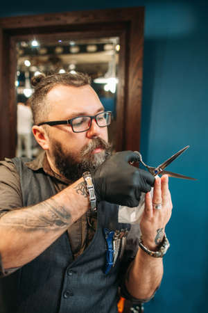 Professional hairdresser teach how to cut hair. Bearded experienced barber holding scissors and check their sharpness, free space. Barbershop, beauty, master class conceptの写真素材