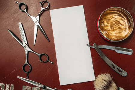 Blank card with barber tools flat lay. Top view on red table with scissors, razor, hair wax and...