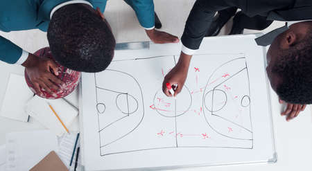 Two american basketball coaches plan and discuss new game strategy. Trainers of student team making scheme of basketball game on the white board.の写真素材
