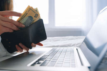 Internet business online, successful startup, freelance work. Unrecognizable woman put money into wallet over laptop, free spaceの写真素材
