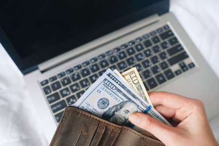 Unrecognizable person hold money and wallet over laptop, closeup. Internet payments, online shopping, buy on website, online bet and casino concept.の写真素材