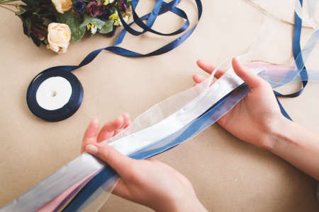 Creative art. Unrecognizable woman hold colorful ribbons on beige background with artificial flowers, close up. Decoration master class from professional. Handmade decor, craft, diy concept.の写真素材