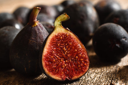 Half of juicy ripe fig fruit on wood closeup. Lot of figs with one cut on foreground. Natural autumn...