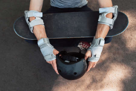 Skateboard halmet, elbow and gloves protection on unrecognizable skateboarder. Head and hands care. Extreme sport injoury. Headwear stuff for skaterの写真素材