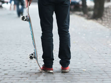 Skateboarder holding skate at street. City life concept of urban culture. One unrecognizable person on red sneakers.の写真素材