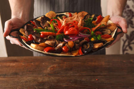 Presentation dish with stewed meat, different kind of vegetables, field mushrooms, laid on lavash and big copper plate, and decorated with sliced onion and pepper. Meal in handsの写真素材