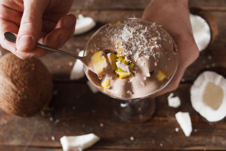 Close up of fruit salad with coconut flakes. Unrecognizable man with spoon of fresh dessert and creamy toppingの写真素材