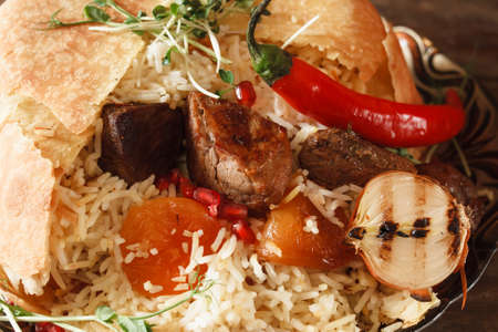 Close up of shah pilaff on big plate. National georgian cuisine, spicy rice with meat under lavash decorated chili pepper, dried apricots and grilled onionの写真素材