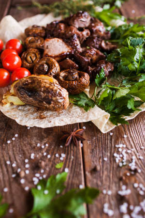 Shish-kebab with grilled vegetables on lavash. Meat, field mushrooms and cherry tomatoes with herbs, barbecue and natural food preparing in restaurant, close upの写真素材