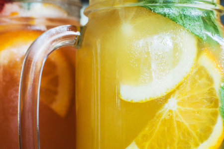 Background of fresh cold cocktails in jars. Close up picture of glass wall of fruit drinks with drops of water, sliced orange shape and mint, refreshment and coolness conceptの写真素材