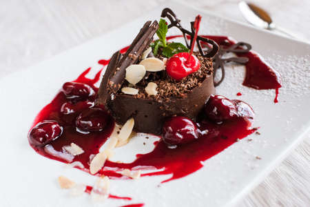 Chocolate cake on white plate with decoration from cherry, almond and mint. Delicious dessert serving in restaurantの写真素材