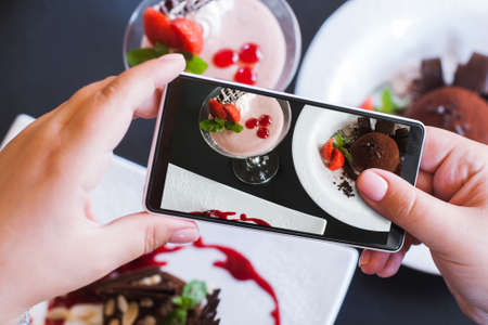 Food photos of delicious desserts by smartphone in restaurant. Creamy strawberry souffle and chocolate fondant, photo shooting and new technology, close up pov pictureの写真素材