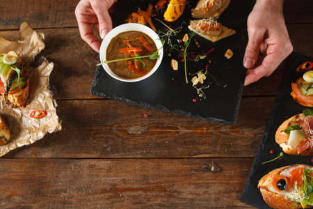 Various canapes on brown wooden background serving in restaurant. Appetizers with paste, salmon, ham and sprats, decorated olive, sliced cucumber and different herbs and spices top viewの写真素材
