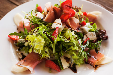 Fresh salad with parma ham, blue cheese and strawberry serving in restaurant. Gourmet cuisine close...