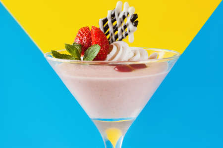 Creamy strawberry dessert on contrast v-shaped blue and yellow background. Sweet fruit souffle decorated with fresh red berry, chocolate and mint, close up pictureの写真素材