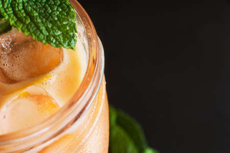 Fruit cocktail partially seen on black background. Fresh cold drink with mint and ice in glass jar, refreshment in hot weather, close up with free spaceの写真素材