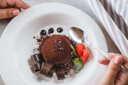 Tasting of delicious chocolate dessert for real gourmet. Customer eats fondant with decoration from strawberry and mint in restaurantの写真素材