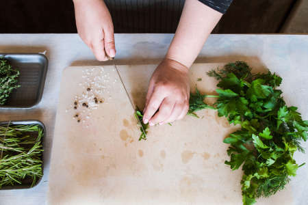 Cook chopping green herbs on wooden cutting desk. Cooking process, healthy organic food and decoration, top view pictureの写真素材