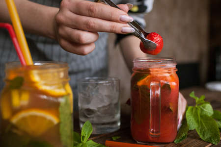 Waiter preparing strawberry cocktail in restaurant. Fresh citrus and berry cold drink with mint and ice on wooden table, concept of refreshment and satisfying thirst, close up pictureの写真素材