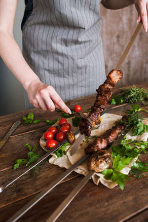 Waiter takes off grilled meat from skewer. Field mushrooms and cherry tomatoes with lavash, barbecue and natural food preparing in restaurantの写真素材