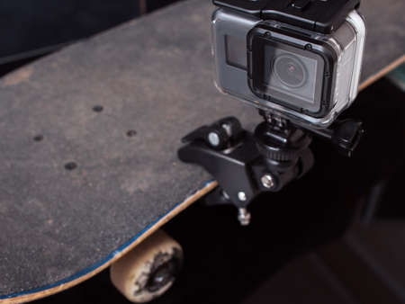 Action camera for professional video shooting of extreme sport tricks, training and competitions, fixed on skateboard rubbed deck on black backgroundの写真素材