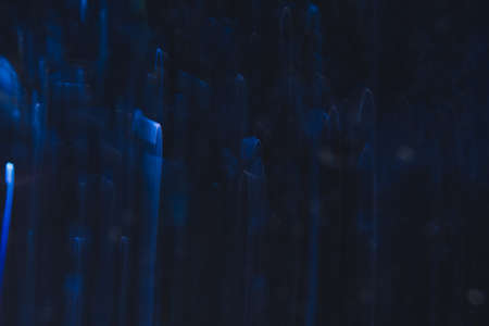 Abstract background of blue bends in motion on black. Bokeh of defocused curves, blurred neon leds, similar to rain drops, backdrop of magic nature aroundの写真素材