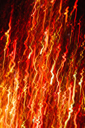 Abstract background of colorful crankles in motion on black. Bokeh of defocused curves, blurred neon yellow and red leds, festive backdrop of fireworks, holidays and celebrationsの写真素材