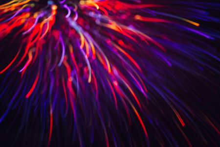 Abstract background of colorful lines in motion on black. Bokeh of defocused curves, blurred red and violet neon leds, festive backdrop of holidays and celebrations, fireworks and saluteの写真素材