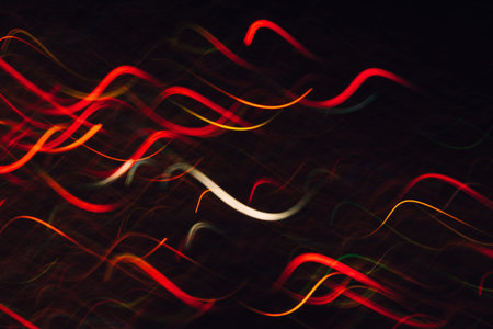 Abstract background of colorful waves in motion on black. Bokeh of defocused curves, blurred neon...