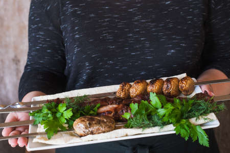 Waiter brings shish-kebab with grilled vegetables on white dish. Meat, field mushrooms and fresh green herbs, barbecue and natural food preparing in restaurantの写真素材