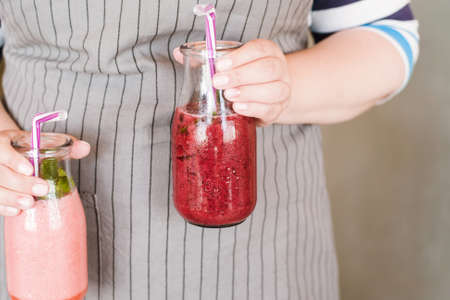 Waiter brings bottles of smoothie to customer. Fruit drinks from strawberry and wineberry with mint, refreshment in summer period, detox, healthy food close up pictureの写真素材