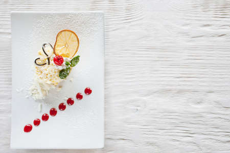 Creamy orange dessert on white wooden table. Delicious cake serving in restaurant with decoration from cherry, chocolate and mint, top view with free spaceの写真素材