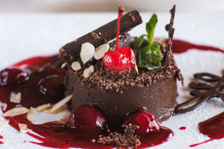 Chocolate cake on white plate with decoration from cherry, almond and mint. Delicious dessert serving in restaurant, close up pictureの写真素材