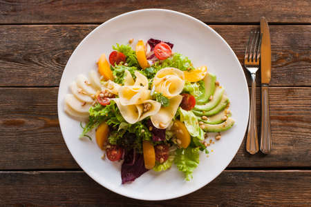 Lettuce salad with cheese and fruits on plate. Fresh vegetables decorated pine nuts, avocado, pearch and pear, serving in restaurant, top viewの写真素材