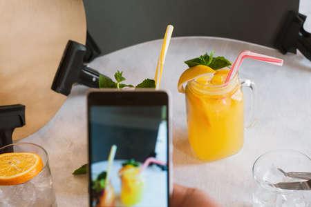 Backstage of food photography of fruit cocktail by smartphone. Making photo of fresh citrus drink with mint and ice, new technology and social networks, close up pictureの写真素材