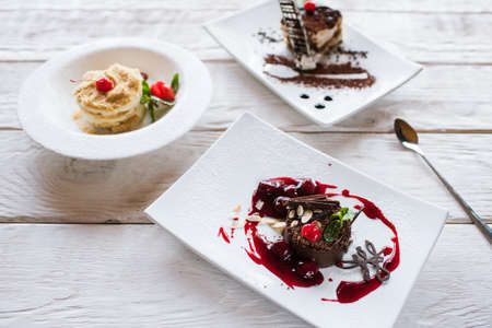 Presentation of delicious desserts in restaurant. Napoleon and chocolate cake with tiramisu serving on wooden table, close upの写真素材