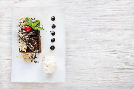 Chocolate pie on white plate with decoration from cherry, almond and mint. Delicious dessert serving in restaurant with ice-cream ball, top view with free space on backgroundの写真素材