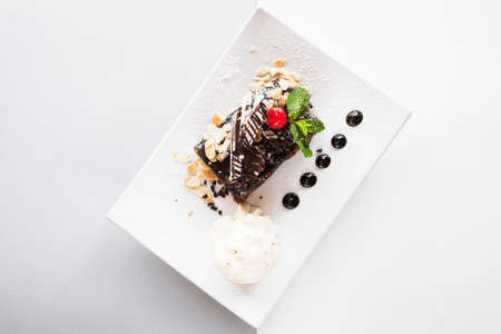 Chocolate pie on white square cut plate with decoration from cherry, almond and mint. Delicious dessert serving in restaurant with ice-cream ball, top view with free space on backgroundの写真素材