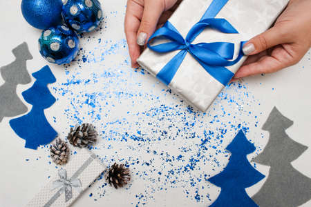 Preparing Christmas decor and gifts. Woman put on table wrapped present, ornament blue balls and felt fir tree nearby with spangles spread around, top view and copy space. Handmade decoration conceptの写真素材