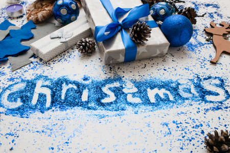 Christmas inscription. Decor and gifts backdrop. Close up wrapped presents and different handmade ornaments, bright spangles spread around. Festive background of holiday decoration conceptの写真素材