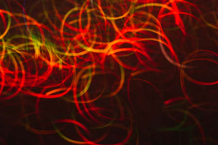 Abstract background of colorful lines in motion on black. Bokeh of defocused curves, blurred neon red, green and yellow leds, festive backdrop of serpantine, holidays and celebrationsの写真素材