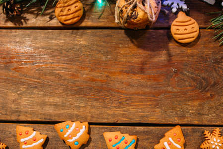 Festive background of Christmas bekary. Top view homemade gingerbread cookies and pine branch on wooden backdrop, free space in middle. Family celebration, New Year traditions and decor conceptの写真素材