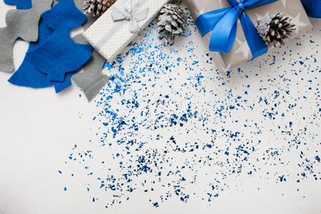 Background of New Year decor and gifts top view. Wrapped in silver paper presents, ornament blue balls and felt fir tree with tinsel spread around, copy space beneath. Handmade decoration conceptの写真素材