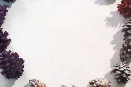 Background of winter holiday decoration. Top view colorful strobilas on white backdrop, free space in middle. Christmas, celebration and New Year decor conceptの写真素材