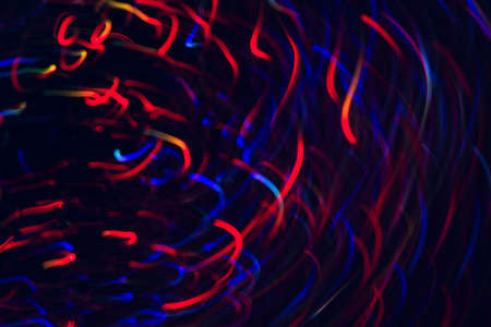 Abstract picture of colorful lines in motion on black background. Bokeh of defocused curves spinning into spiral, blurred neon blue and red leds, festive backdrop of city lightsの写真素材