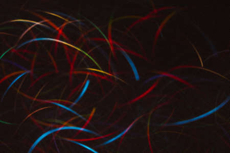 Abstract background of colorful lines in motion on black. Bokeh of defocused curves, blurred neon blue, red and yellow leds, festive or business backdrop of serpantine, holidays and celebrationsの写真素材