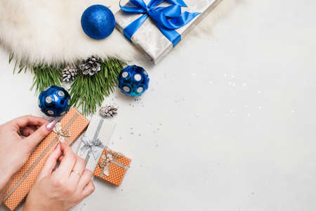 Holiday preparation. Christmas and New Year. Unrecognizable woman wrapping present boxes, handmade decoration, ornament blue balls and pine branch laying on table nearby, top view with copy spaceの写真素材