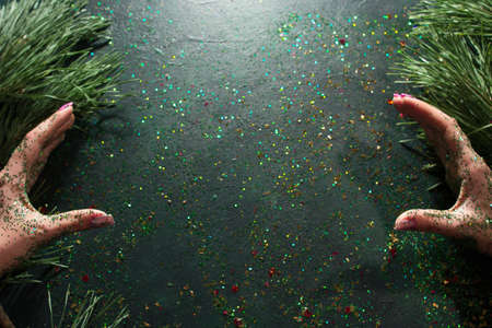 Backdrop for representing Christmas greeting. Top view holiday sparkled hands of woman imitated of holding smth on black glittering background with pine. Celebration and congratulation conceptの写真素材