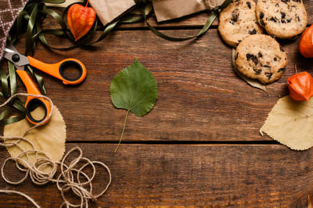 Autumn festive background top view. Chocolate cookies with partially seen small gifts, scissor and bands laying on wooden table with free space in the middleの写真素材